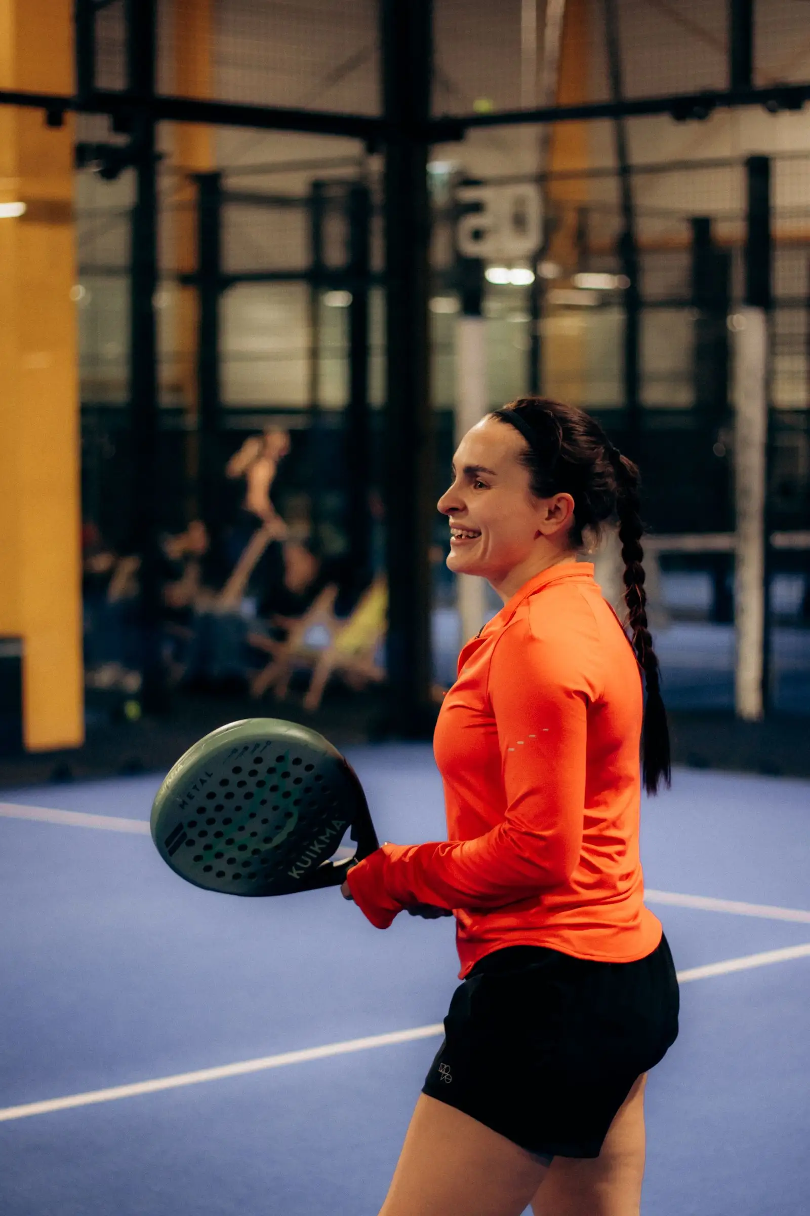 Une joueuse souriante, raquette en main, sur un terrain de padel